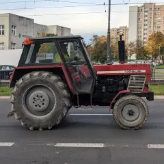 Czerwony Ursus 1954, model 902, jedzie ulicą. W tle budynki mieszkalne i drzewa.
