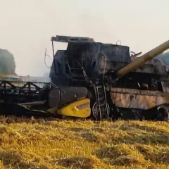 Pożar kombajnu na polu. Maszyna jest mocno zniszczona, widać dym i strażaka w akcji.