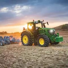 Zielony traktor John Deere Mannheim orze pole o zachodzie słońca.