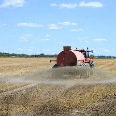 Czerwony traktor z beczkowozem rozprowadza odpad z biogazowni na polu.
