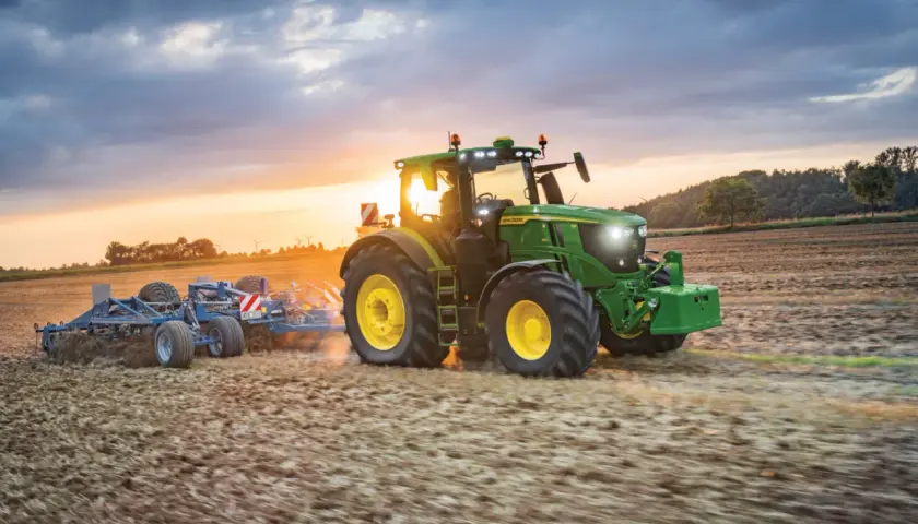 Zielony traktor John Deere Mannheim orze pole o zachodzie słońca.