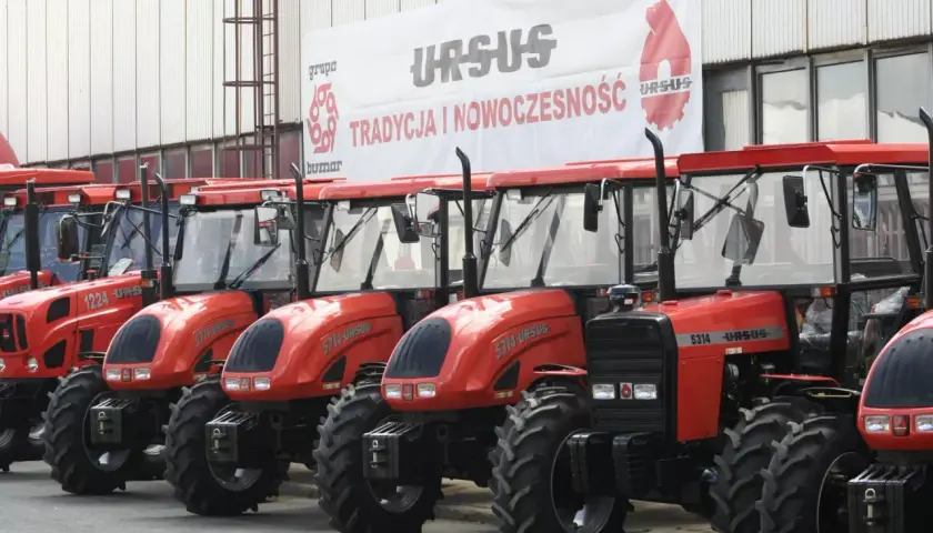 Rząd czerwonych traktorów Ursus, z banerem "Tradycja i Nowoczesność" w tle. Ursus sprzedany, ale maszyny czekają na nowe życie.