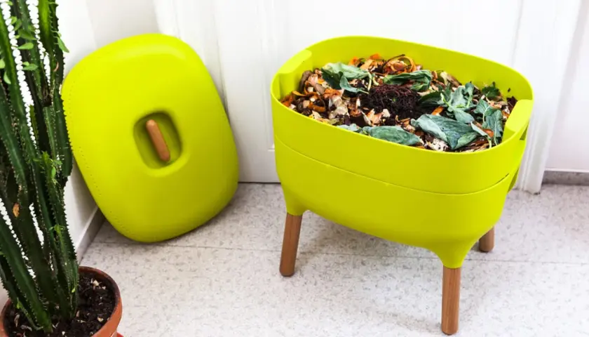 Zielony kompostownik na balkonie, pełen resztek organicznych, obok stoi jego pokrywa.