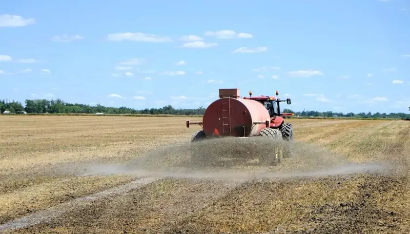 Czerwony traktor z beczkowozem rozprowadza odpad z biogazowni na polu.