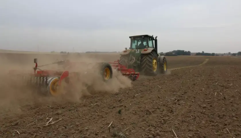 Traktor z agregatem uprawowym wykonuje uprawę bezorkową, wzbijając tumany kurzu na polu.