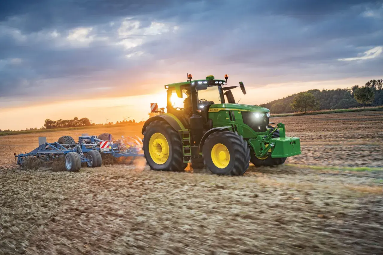 Zielony traktor John Deere Mannheim orze pole o zachodzie słońca.