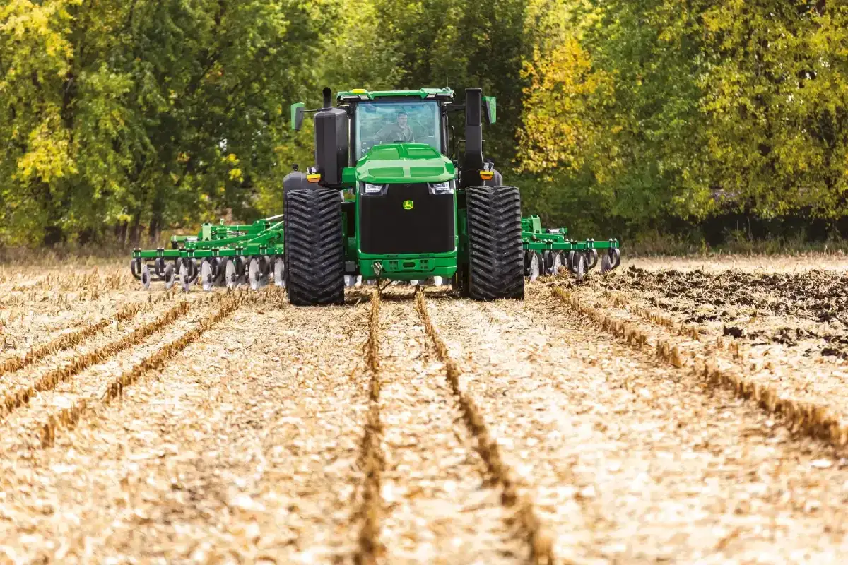 Potężny John Deere 9RX 830 z pługiem pracuje na polu, przygotowując ziemię do siewu.