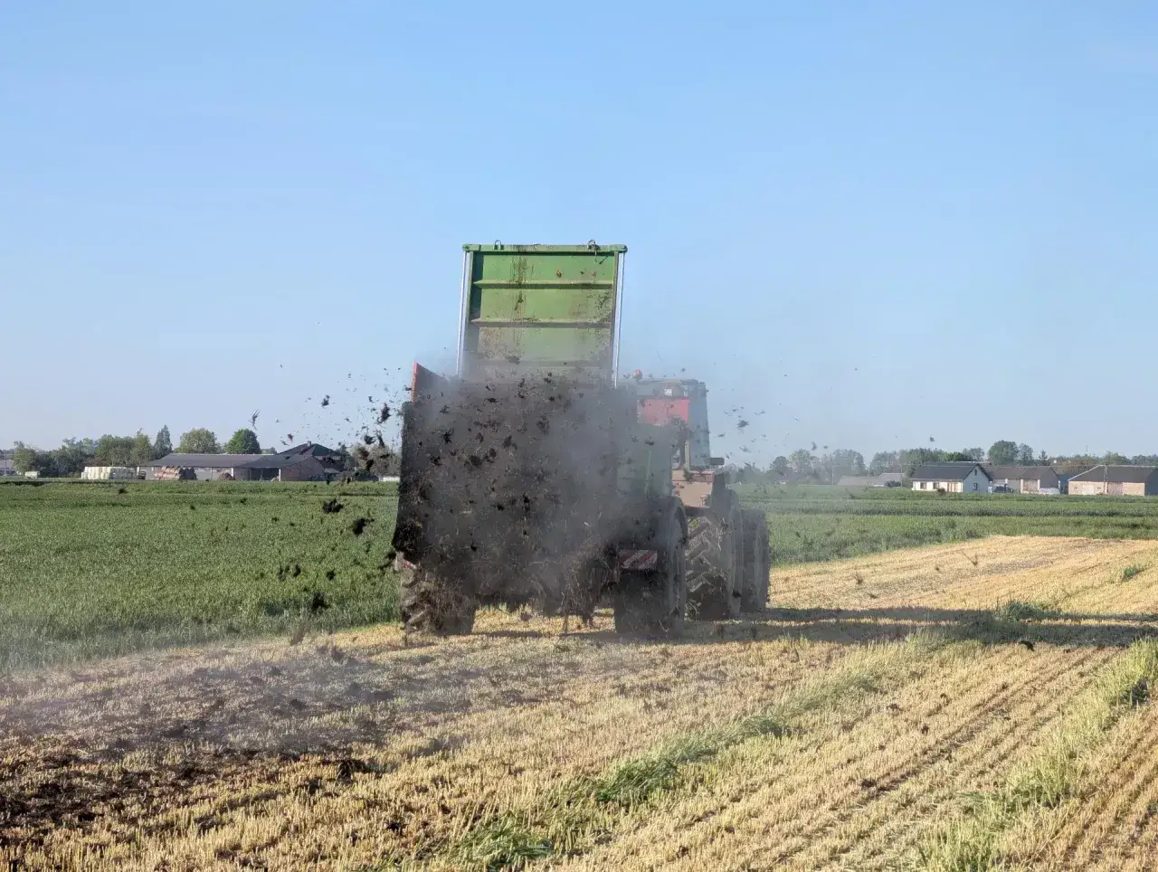Traktor z przyczepą rozsypuje obornik na polu. To ważny termin wywozu obornika, przygotowujący ziemię do kolejnych upraw.