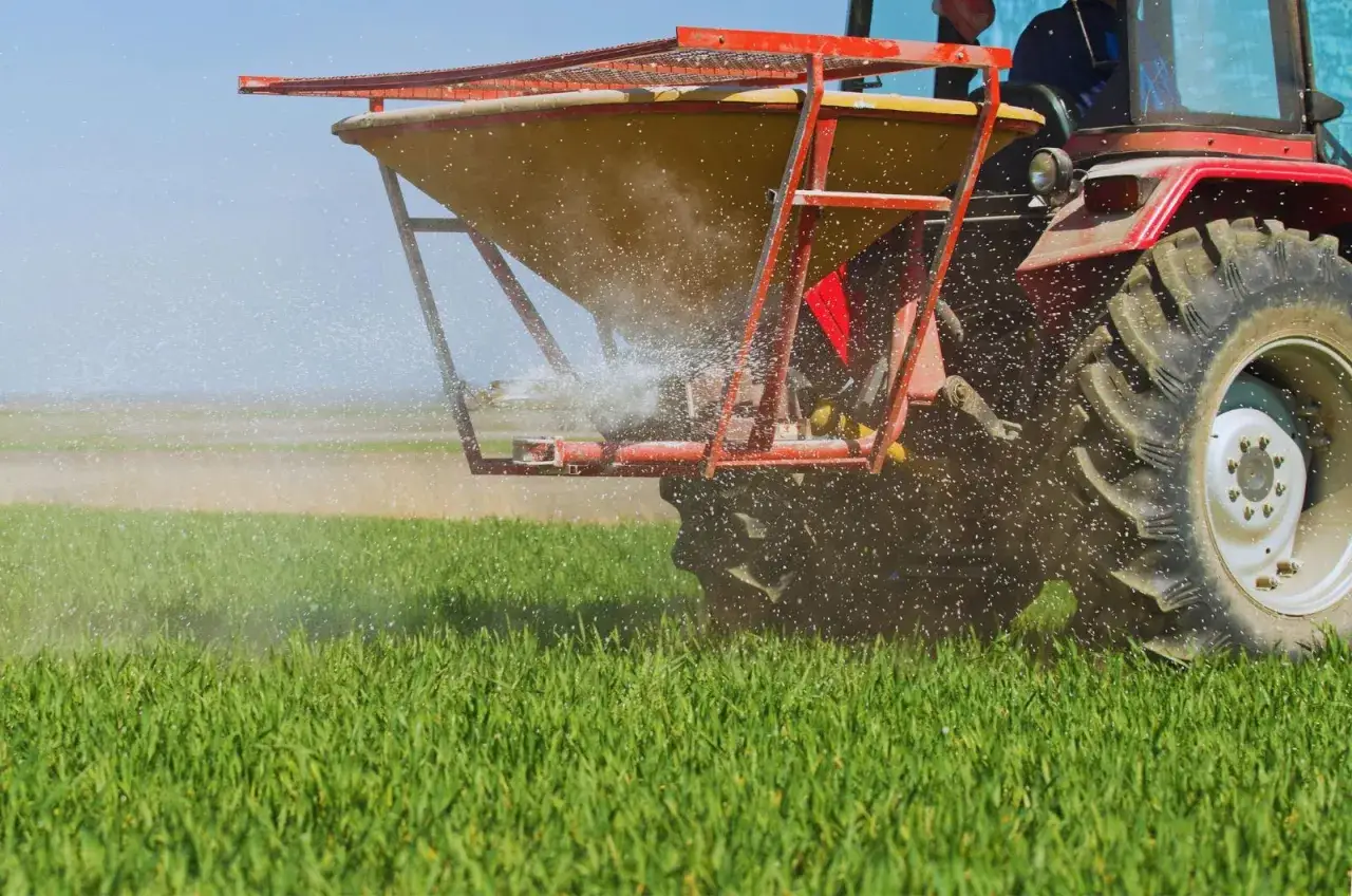 Czerwony traktor rozsiewa wapno posodowe na zielonym polu, poprawiając jakość gleby dla przyszłych plon&oacute;w.