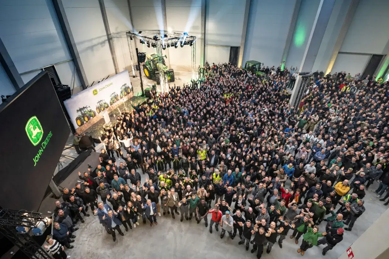 Wielka grupa ludzi świętuje sukces John Deere Mannheim. Na scenie ciągnik, a w tle logo firmy.