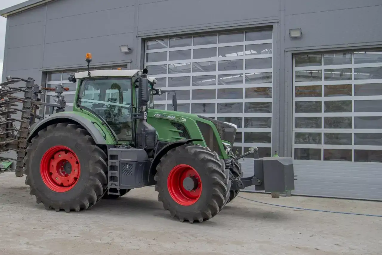 Zielony traktor Fendt z dużymi, czerwonymi felgami przed halą. Ile motogodzin to dużo dla takiego potwora?
