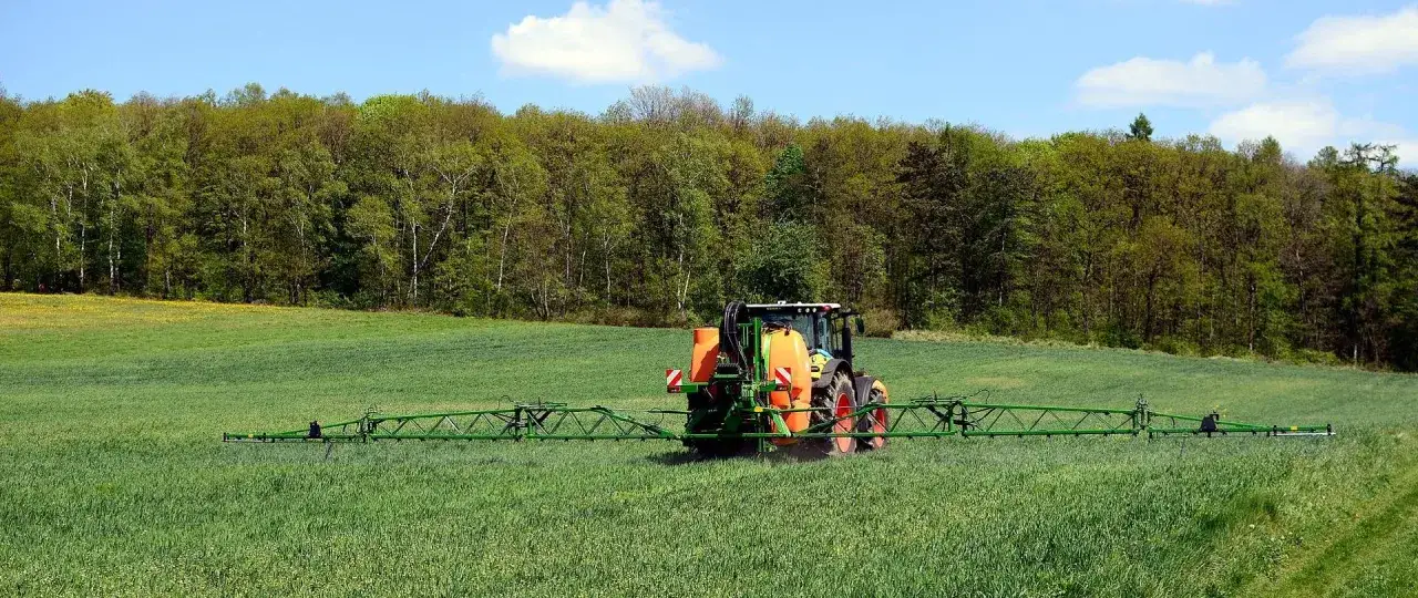 Traktor z opryskiwaczem na zielonym polu. Czy można pryskać rano? Tak, jeśli pogoda sprzyja i nie ma wiatru.